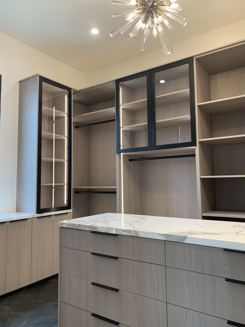 Custom walk-in closet with backlit shelving, a marble-top island, and a chandelier, San Diego