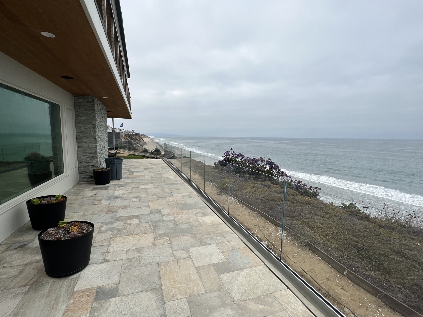 Ocean-view paver patio with black planters and a frameless glass railing on a coastal San Diego home